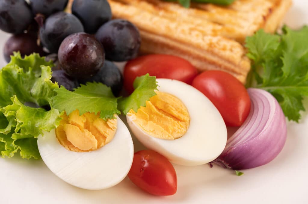 el desayuno consiste en pan huevos duros aderezo de ensalada de uva negra tomates y cebollas en rodajas